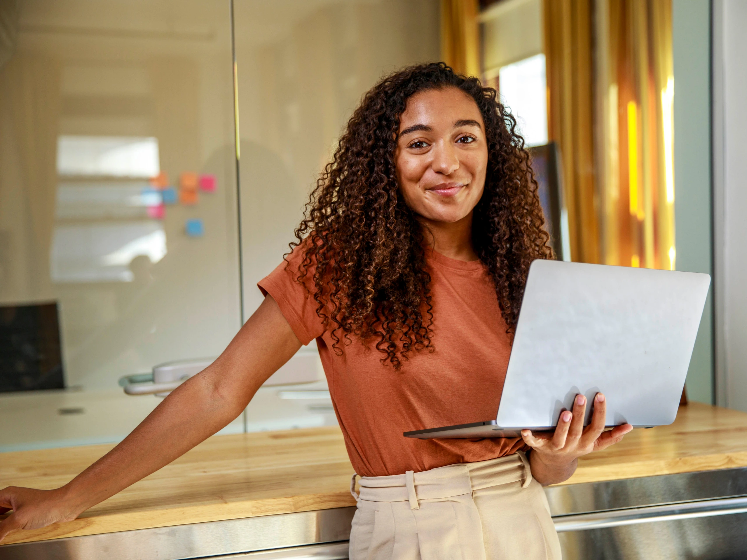 Junge Frau steht mit Laptop in der Hand in einem Büro