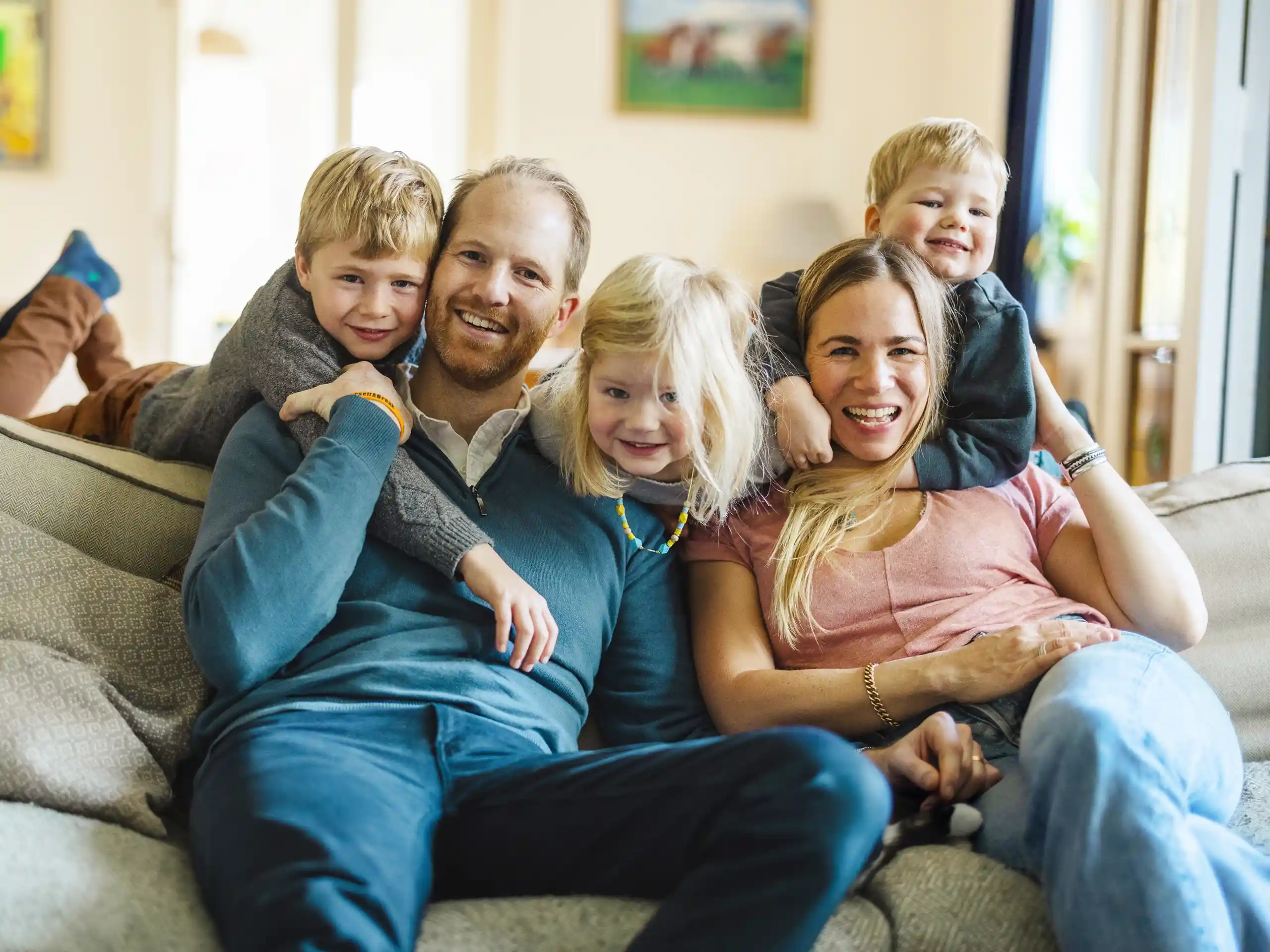 Familie sitzt gemeinsam auf einem Sofa und lächelt in die Kamera.