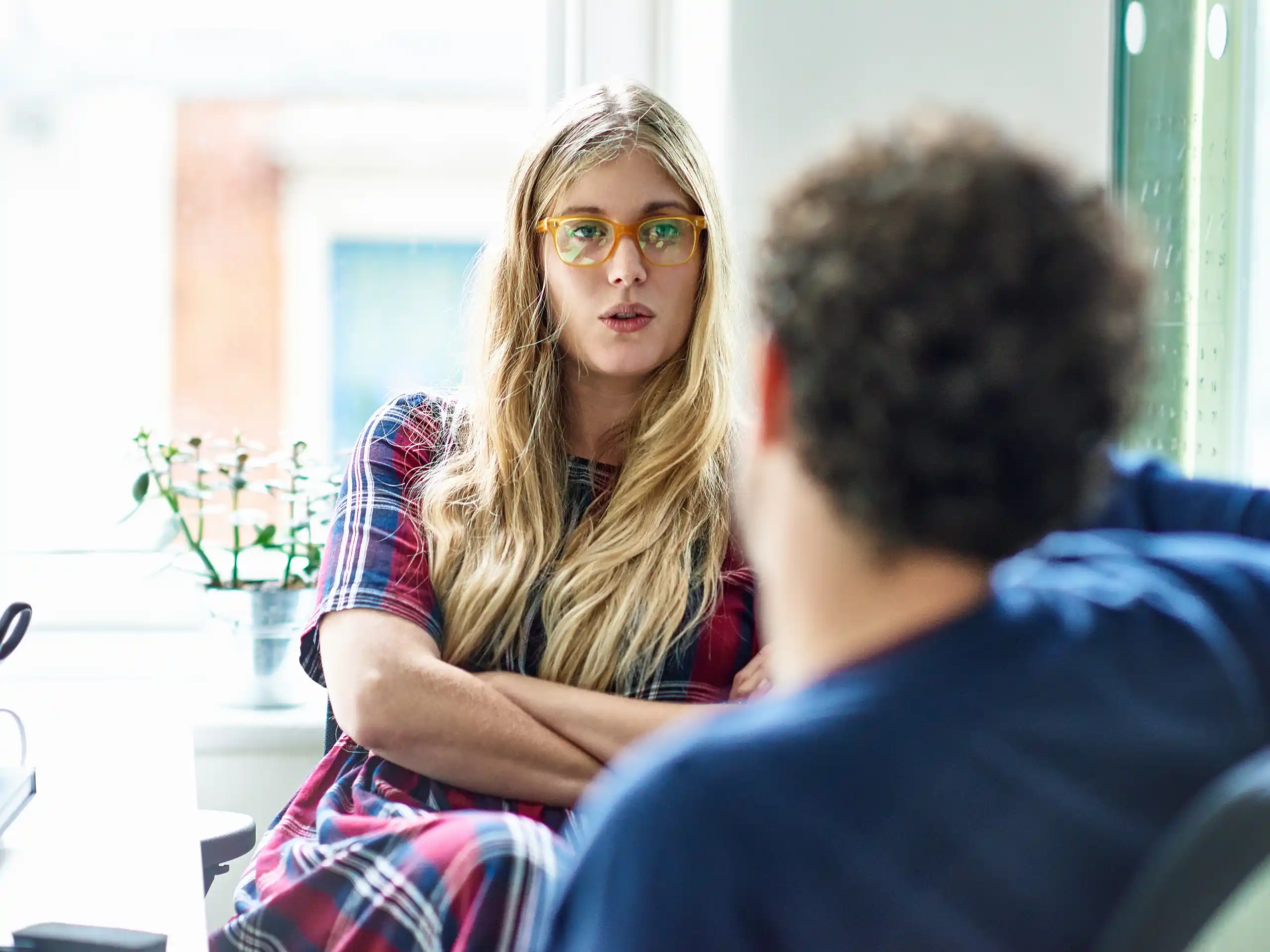 Frau sitzt mit verschränkten Armen und spricht mit einer Person.
