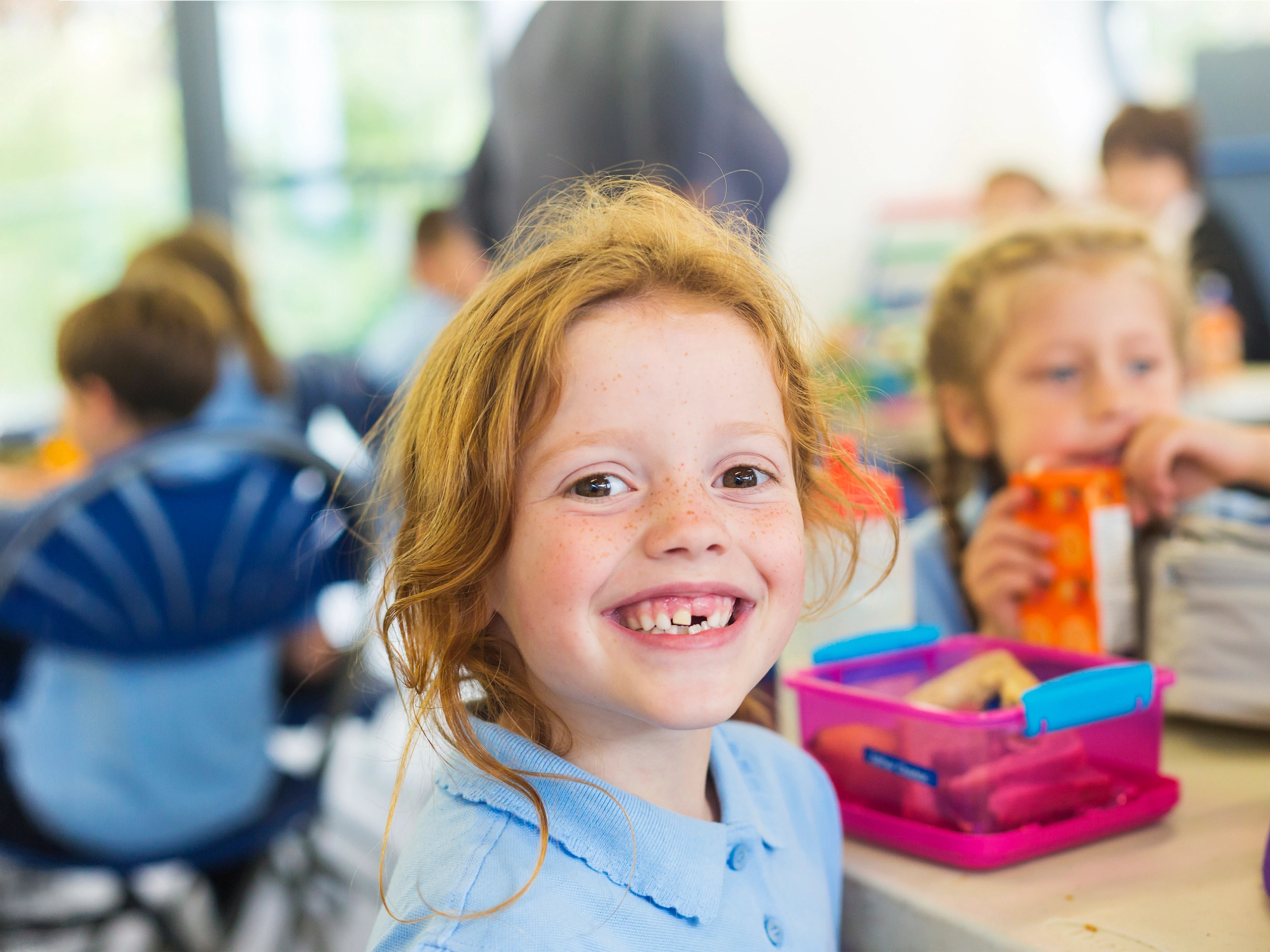 Fröhliches Mädchen mit Zahnlücke in Schulmensa