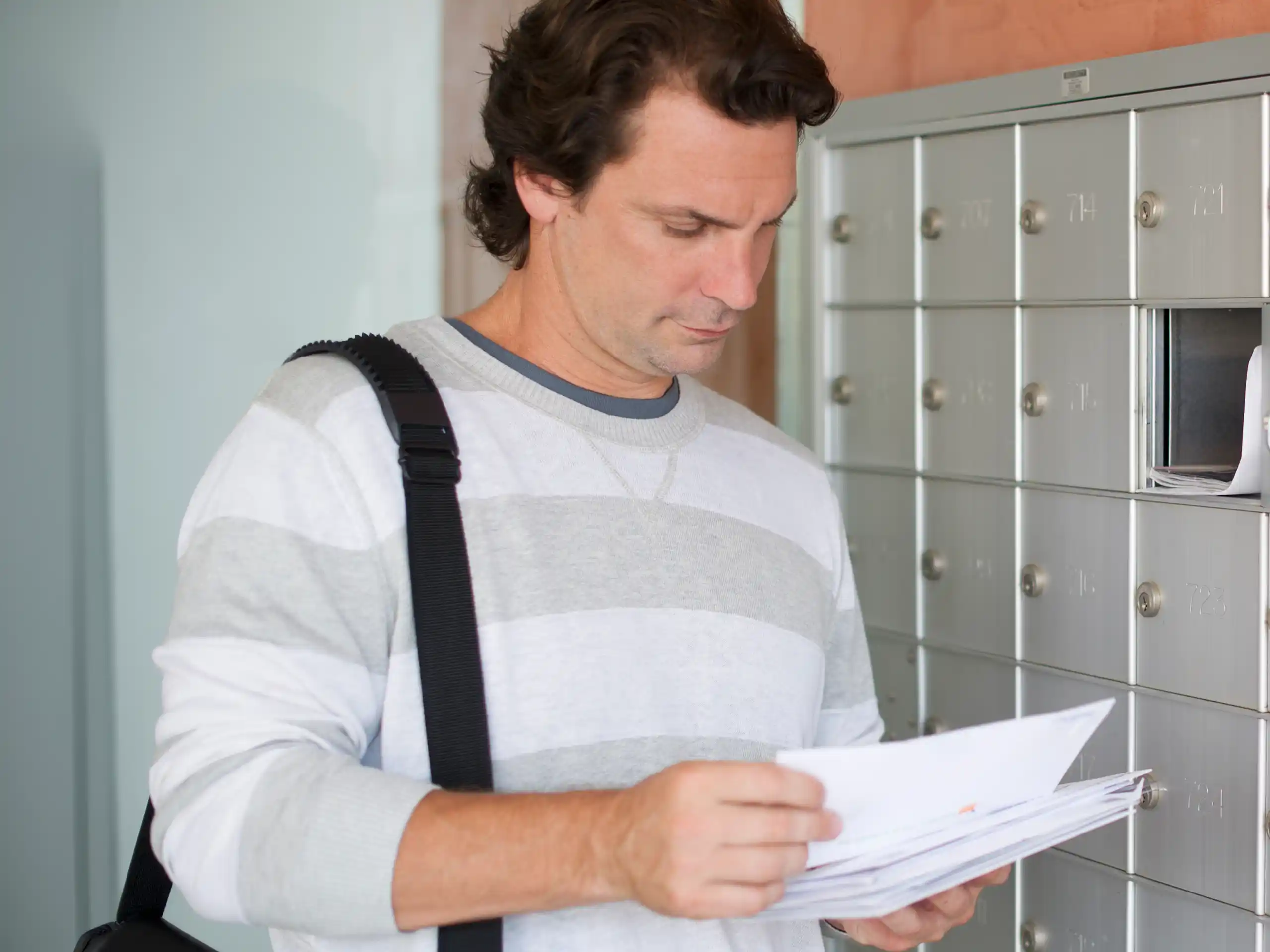 Mann steht vor Briefkästen und prüft mehrere Briefe in der Hand.